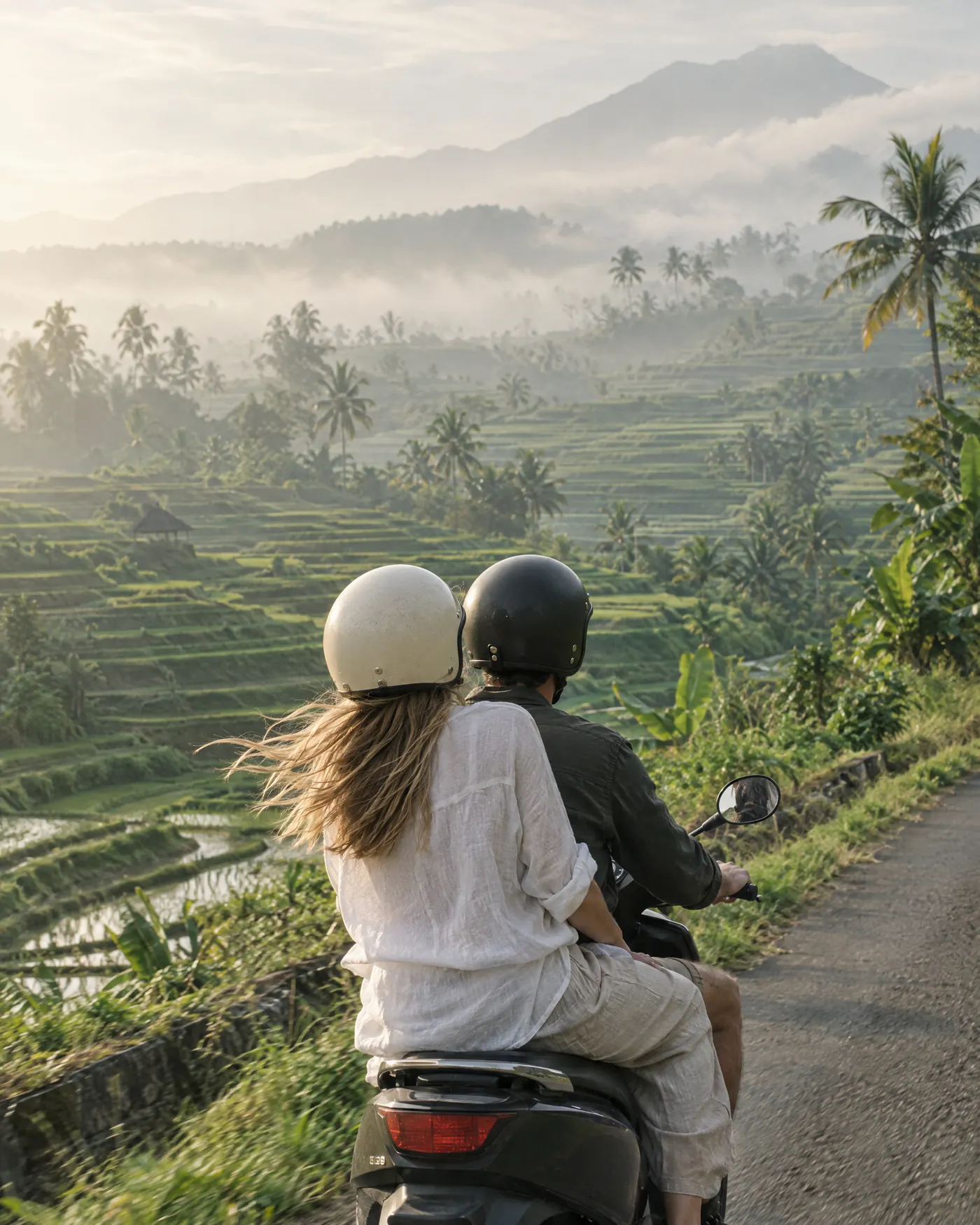 Two friends riding a scooter past misty rice terraces in Bali